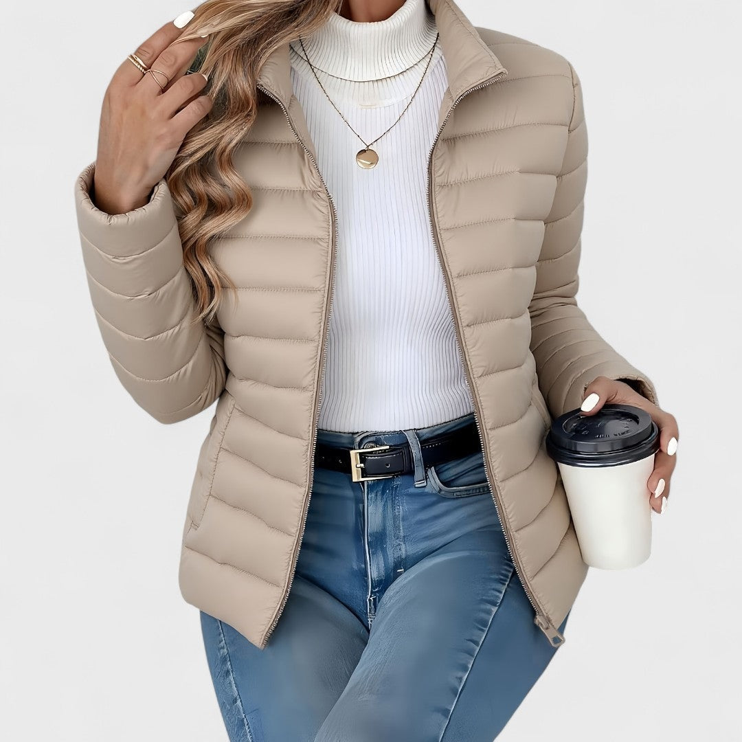 Taupe quilted jacket with a stand collar and open zipper, shown with long sleeves and a white turtleneck.