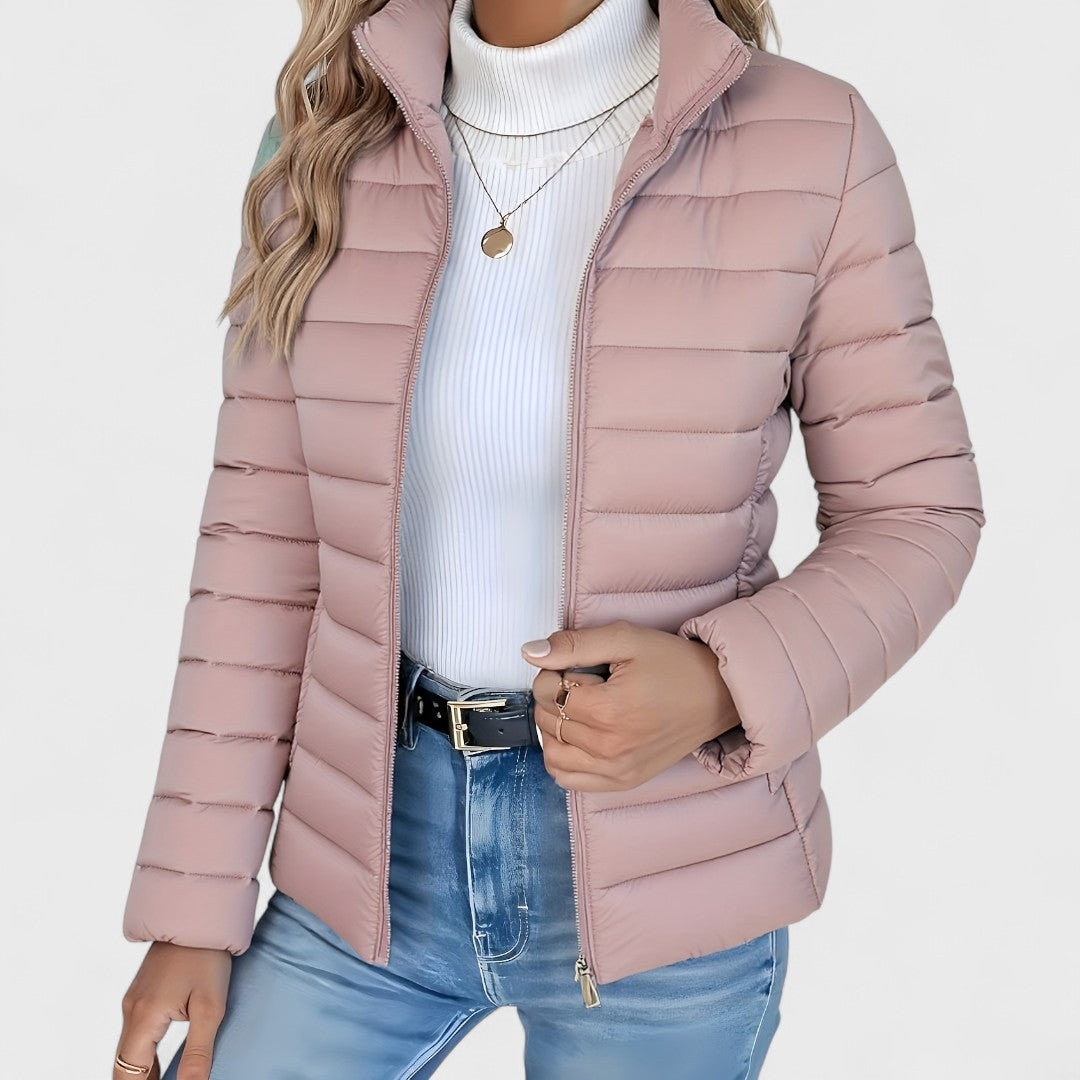 Dusty pink quilted jacket shown from the front with the zipper closed near the bottom and one hand at the fastening.
