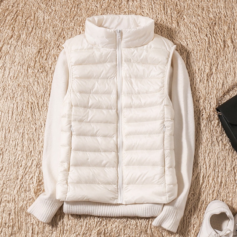 White quilted puffer vest styled over a white sweater, showing the raised collar, full front zipper, and pocket openings.