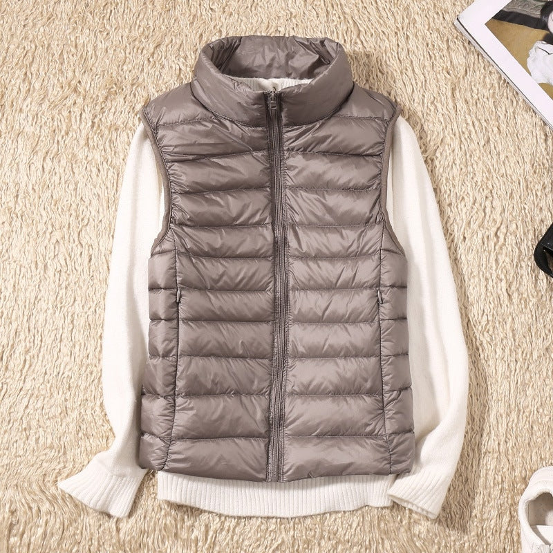 Taupe quilted puffer vest over a white sweater, showing the full front zipper, horizontal quilting, and sleeveless cut.
