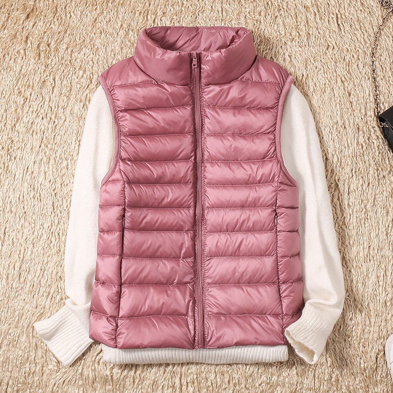 Dusty pink puffer vest styled over a white sweater, with horizontal quilt lines and two side pockets visible.