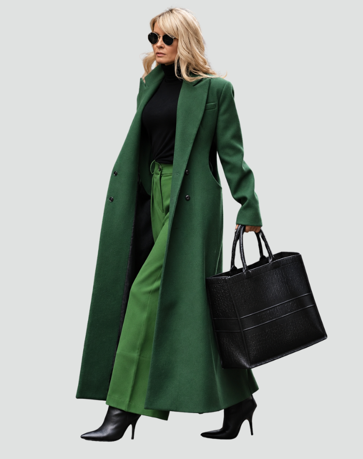 Deep green long coat shown from a side angle with its front open, styled with black clothing, ankle boots, and a structured tote.