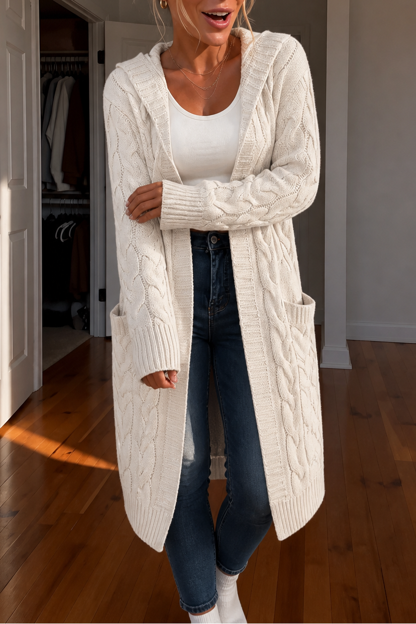 Long cream cable knit cardigan worn open over a white top and dark jeans, with the hood resting behind the neck.