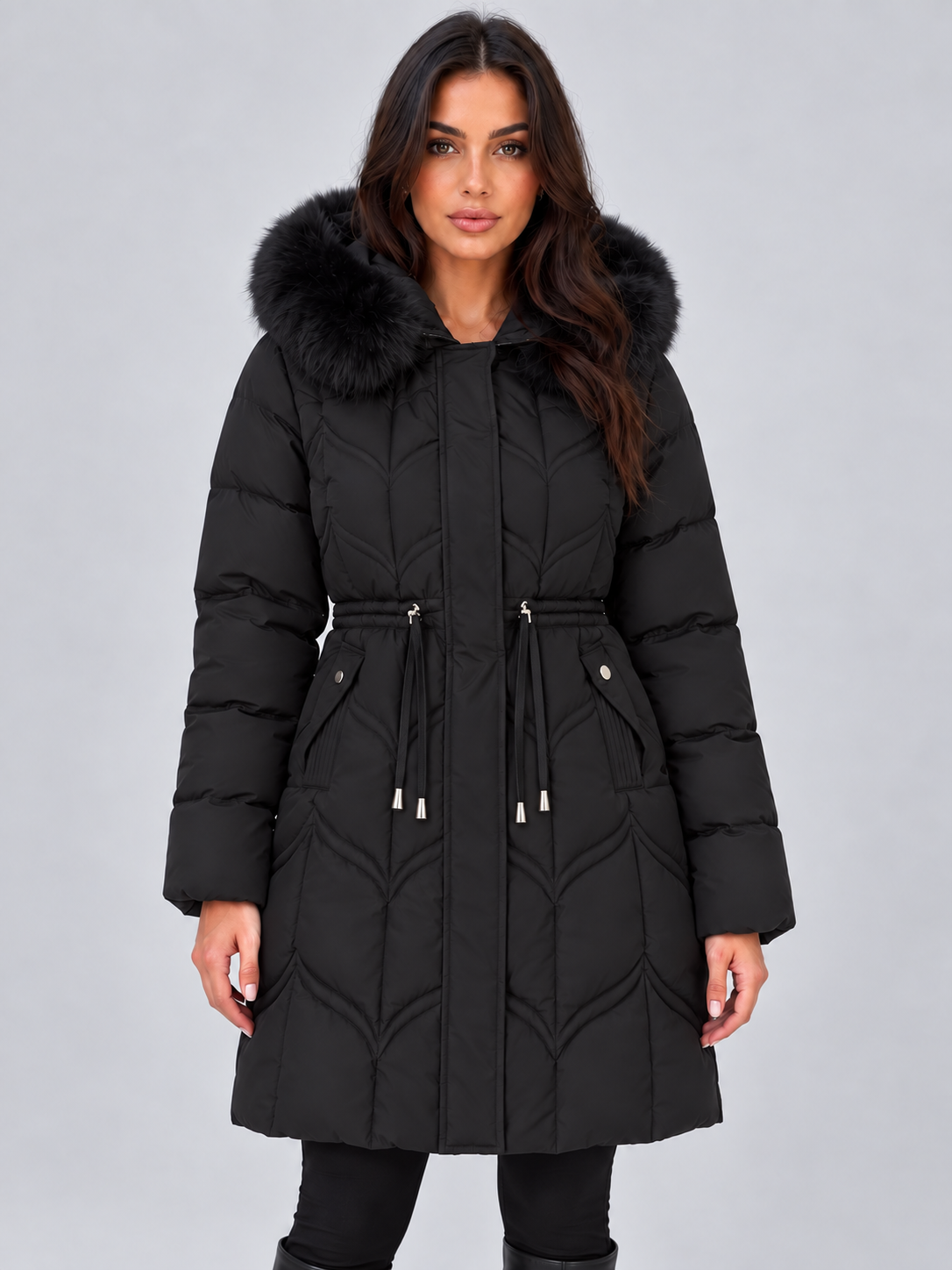 Front view of a long black hooded puffer coat with faux fur trim, quilted panels, adjustable drawstring waist, concealed front closure, and multiple pockets.