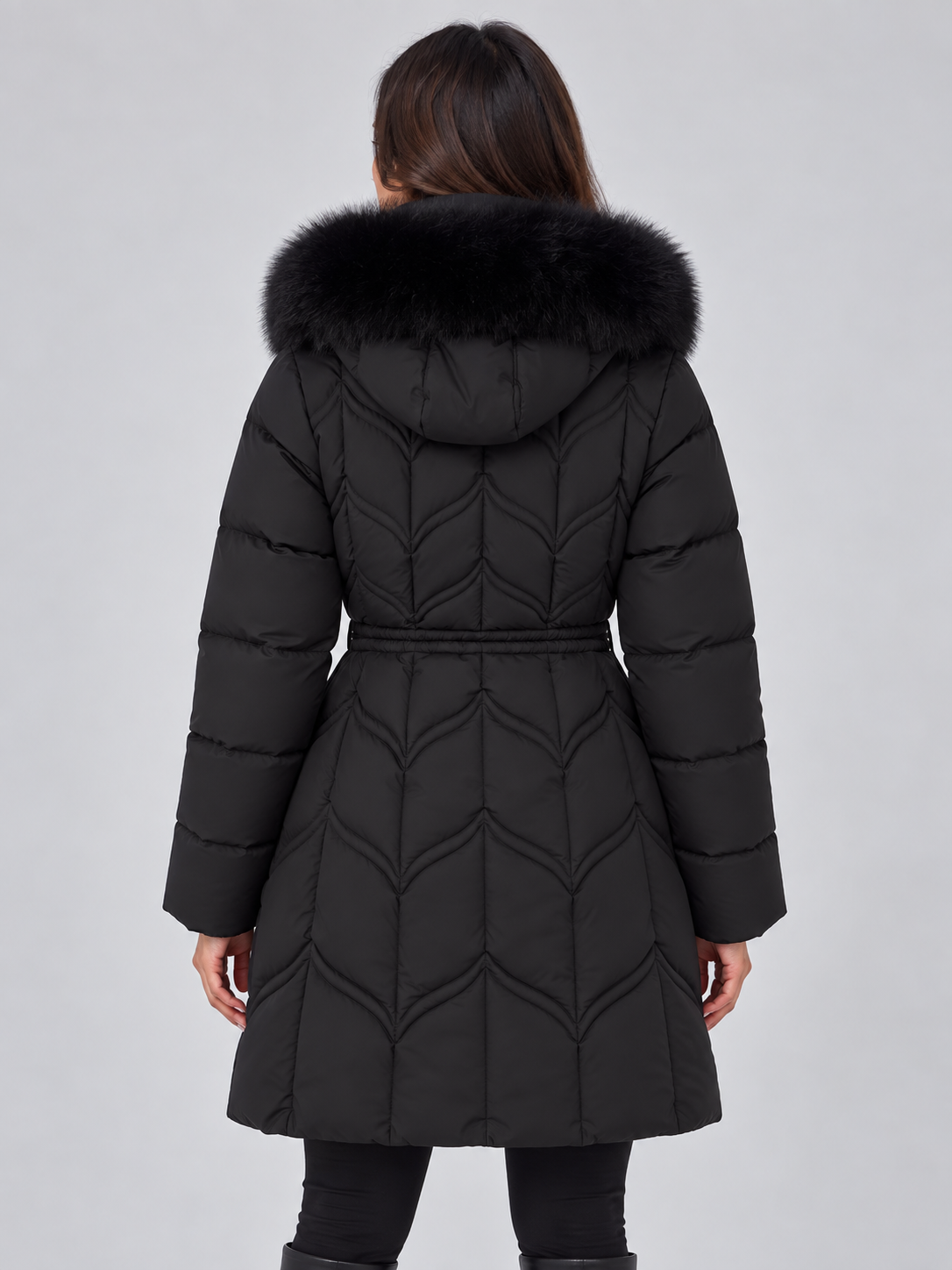 Back view of the black long puffer coat showing its fur-trimmed hood, fitted drawstring waist, long sleeves, and decorative quilted pattern.