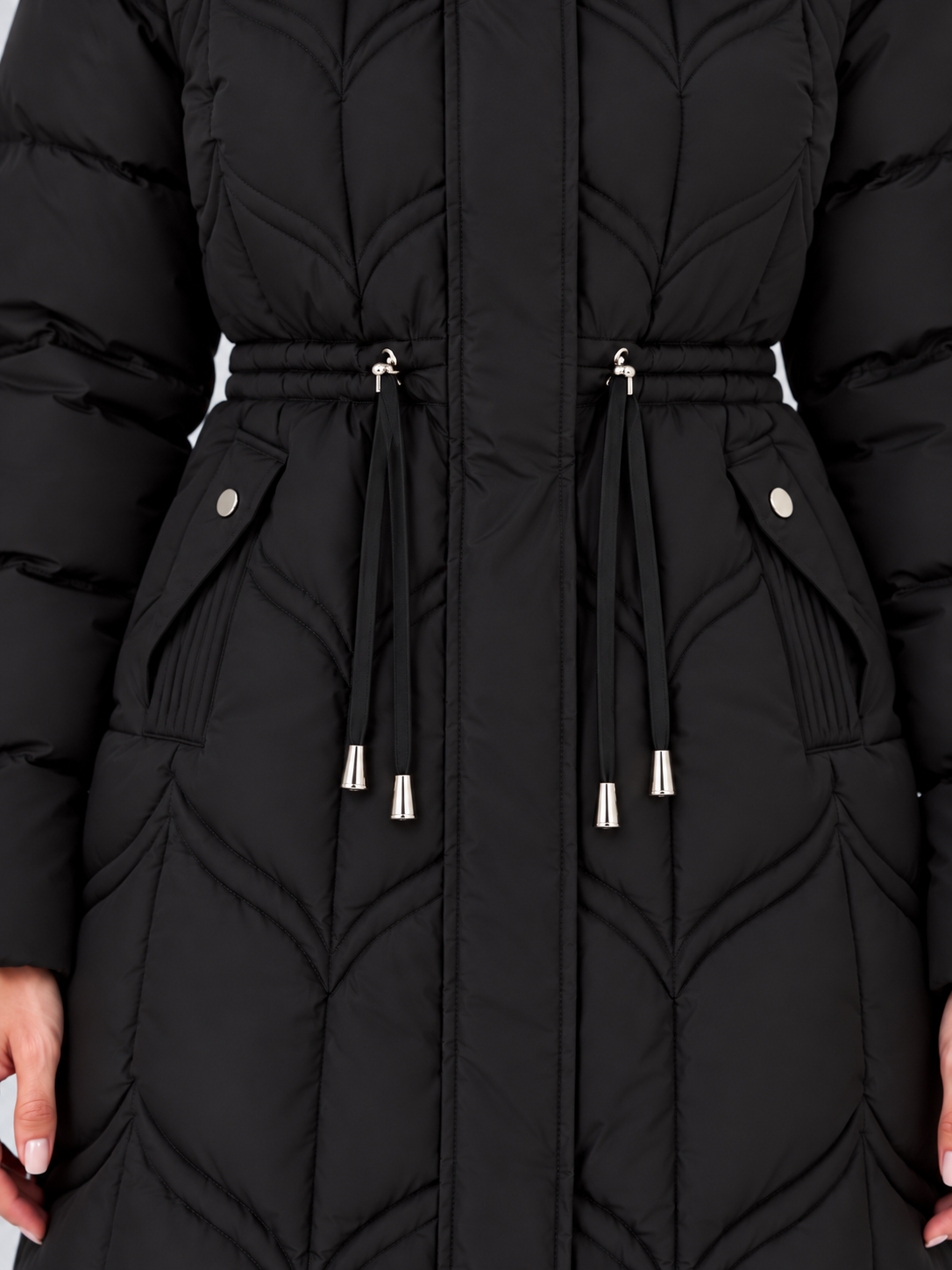Close-up of the black coat’s adjustable drawstring waist, concealed front closure, quilted panels, hanging toggles, and flap-covered pockets.