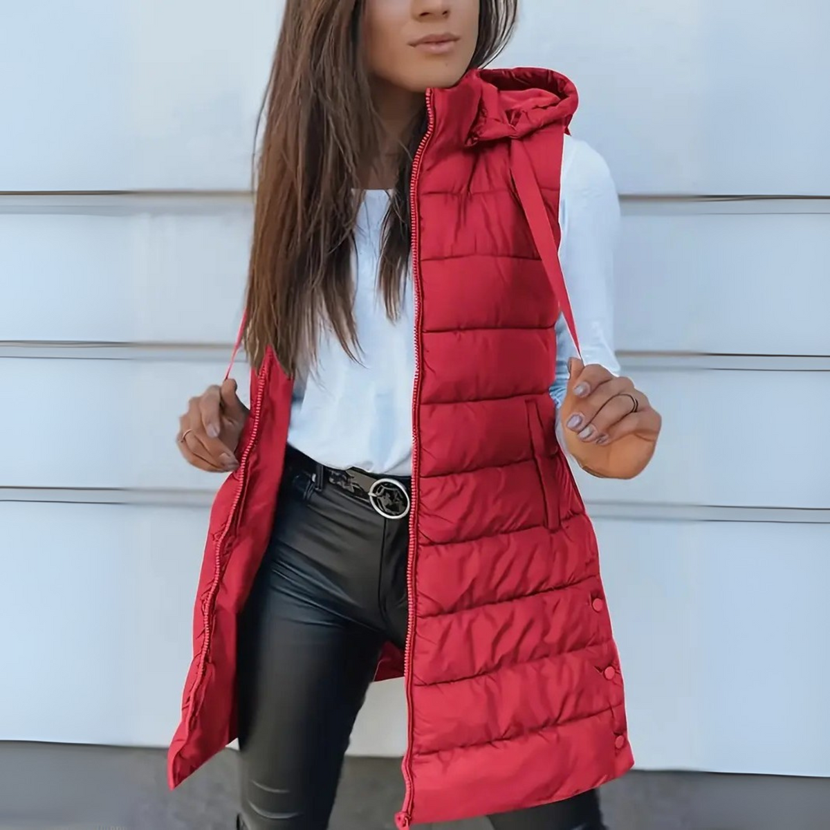 Bright red long hooded puffer vest worn open, with the hood, front zipper, sleeveless shape, and lower snap fasteners visible.