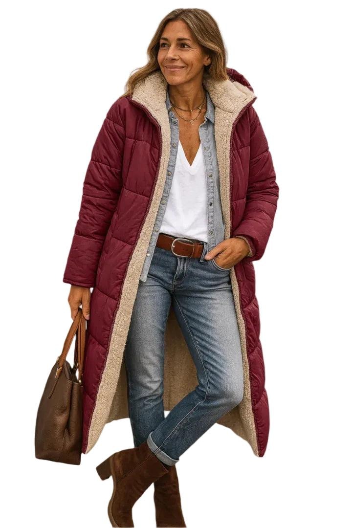 Model wearing a burgundy long quilted coat with a plush-lined hood and carrying a handbag beside the extended hem.