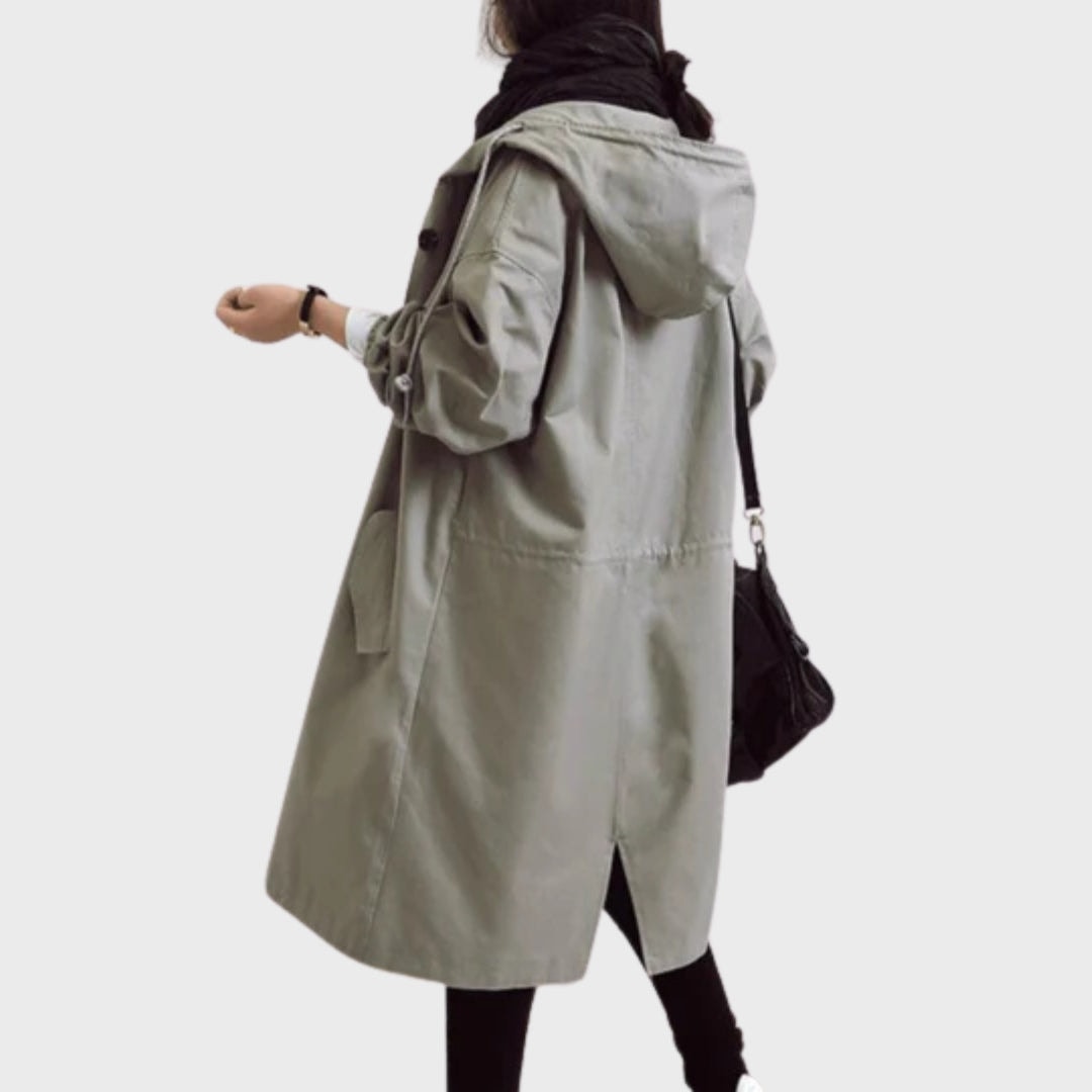 Back view of the light taupe hooded rain coat, showing its long relaxed shape, hood, rear seam, and back slit.