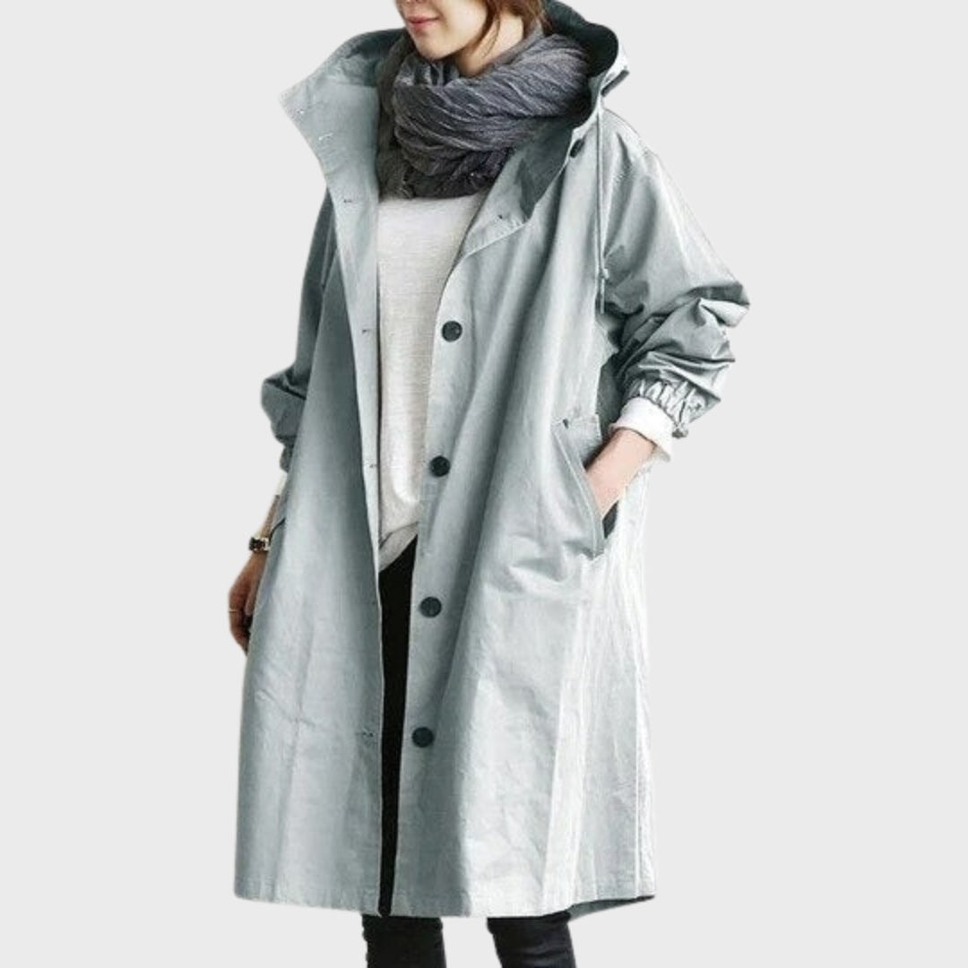 Front view of the rain coat in pale blue-grey, with an open hood, long sleeves, button closure, and angled side pockets.