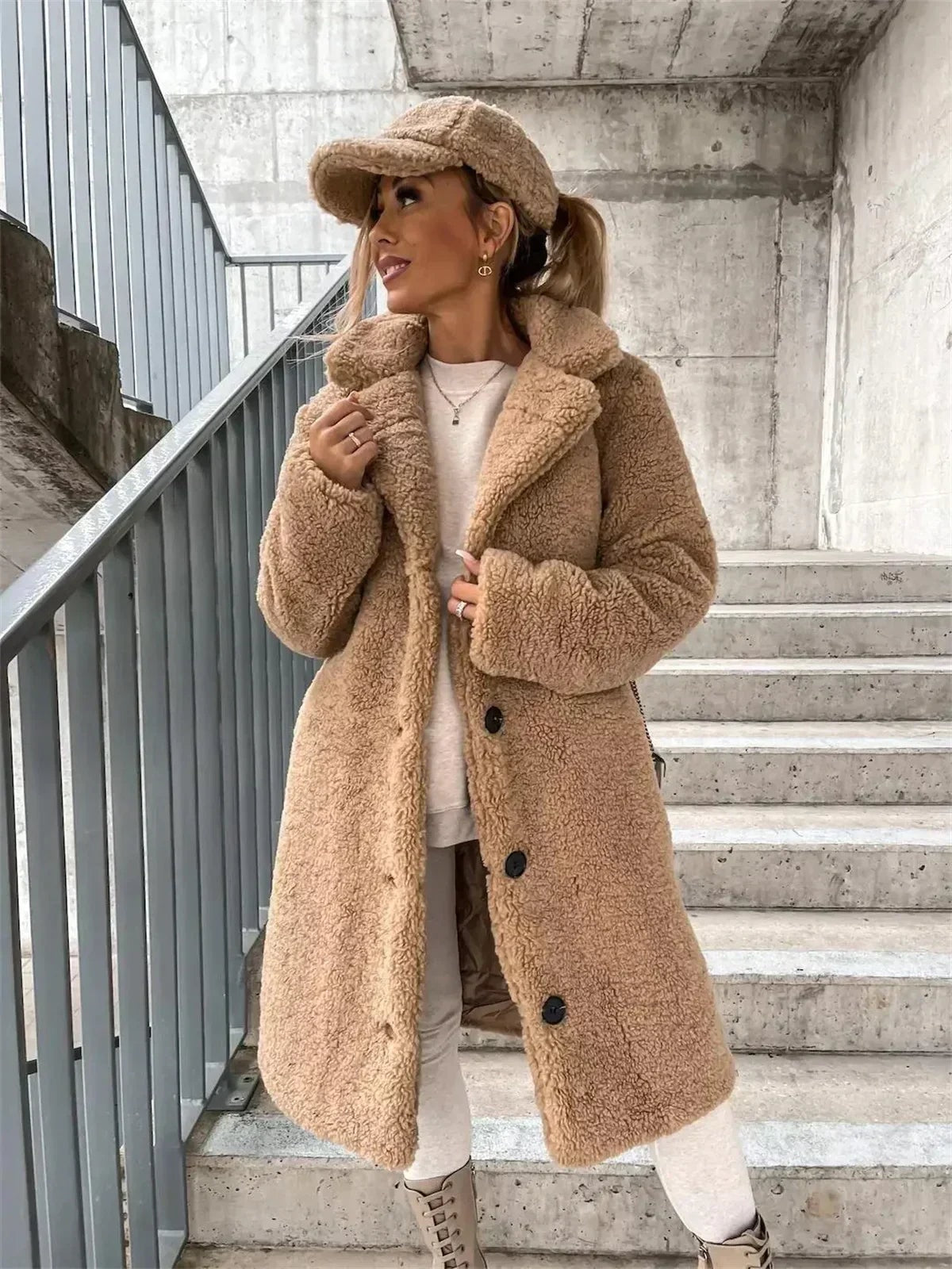 Tan long teddy coat styled open over light layers, showing its plush notched collar, long sleeves, front buttons, and side pockets.