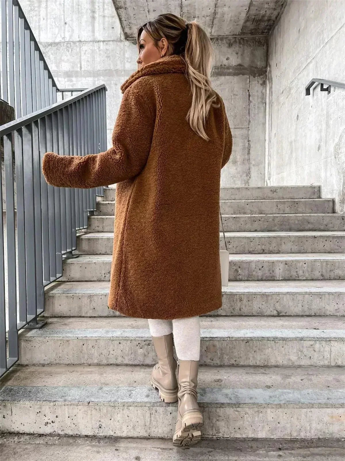 Back view of the tan teddy coat, showing its long straight silhouette, full back coverage, long sleeves, and raised collar.