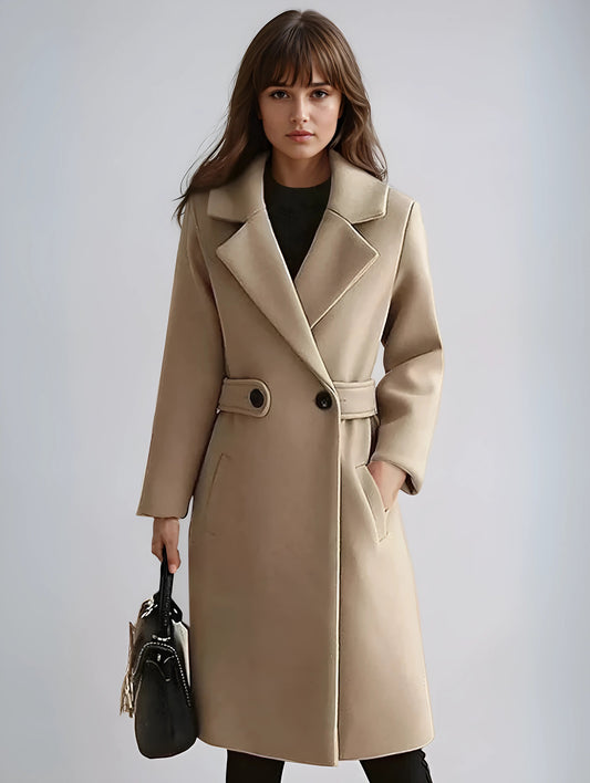 Beige long trench coat with wide notched lapels, double-breasted buttons, waist tab, and front pockets, styled with a black outfit.