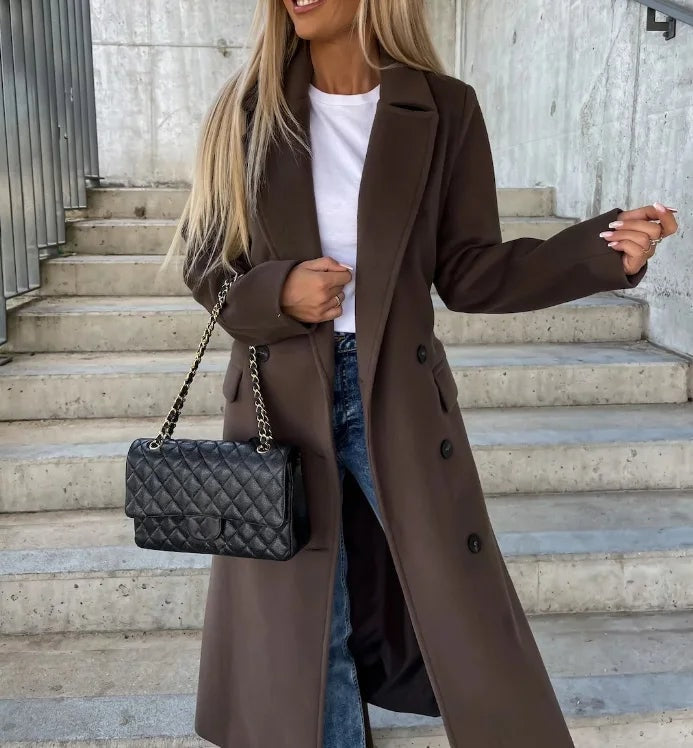 Dark brown longline double-breasted coat with notched lapels and long sleeves, styled open over a white top and jeans.