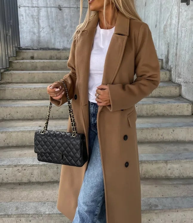 Camel longline double-breasted coat with notched lapels and visible front buttons, shown layered over a white top and jeans.