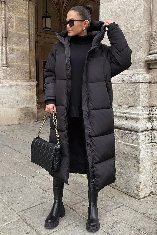 Black longline hooded puffer coat styled with a high-neck black outfit, tall boots, and a quilted handbag; the raised hood highlights the generous coverage.