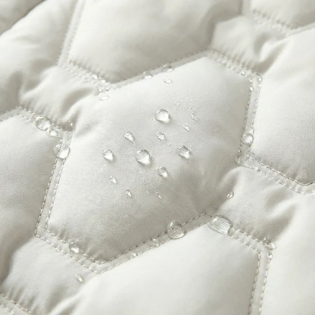 Close-up of white quilted coat panels with water droplets gathered across the stitched surface.