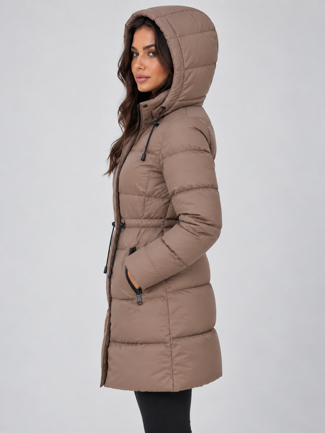 Side profile of the taupe hooded puffer coat highlighting its longer silhouette, raised hood, high neckline, and adjustable waist.