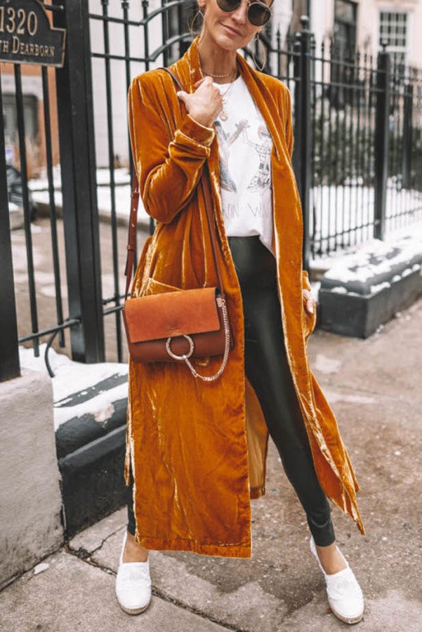Closer outdoor view of the mustard calf-length coat, showing its ruched sleeve and long open front.