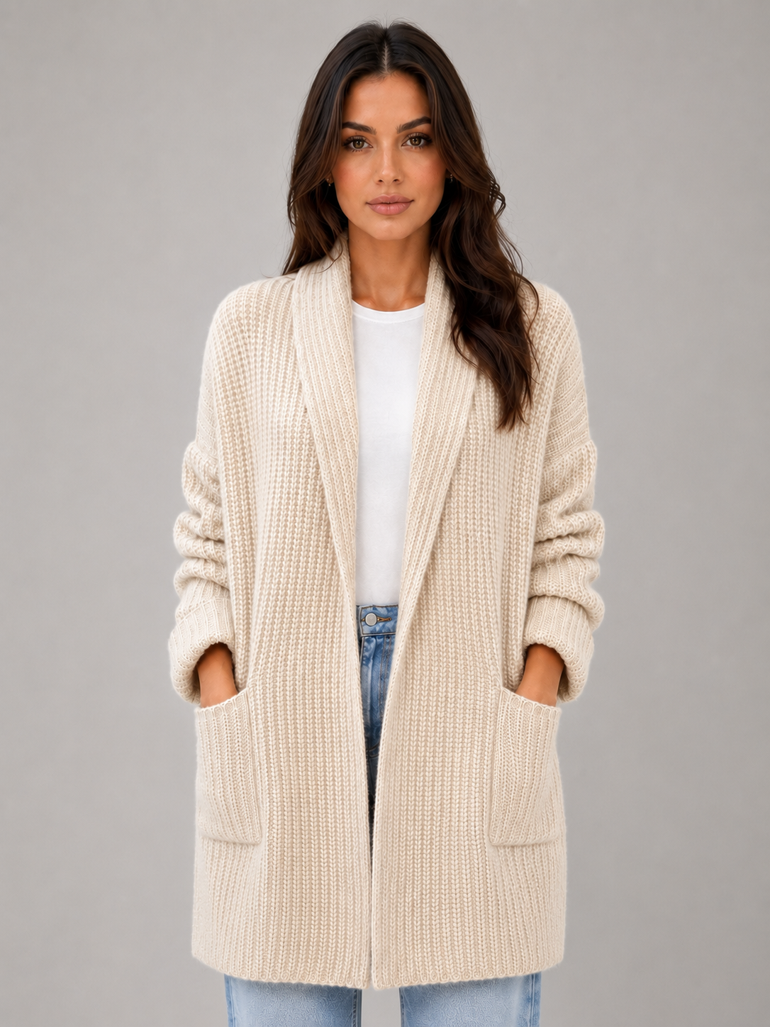 Front view of a cream longline open-front cardigan with long sleeves and two front patch pockets, styled over a white top and jeans.