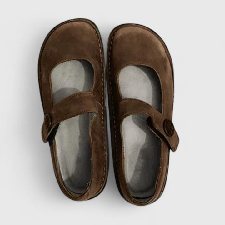 Brown Mary Jane flats viewed from above, showing the rounded-square toe shape, open vamp areas, and adjustable straps with button-like side details.