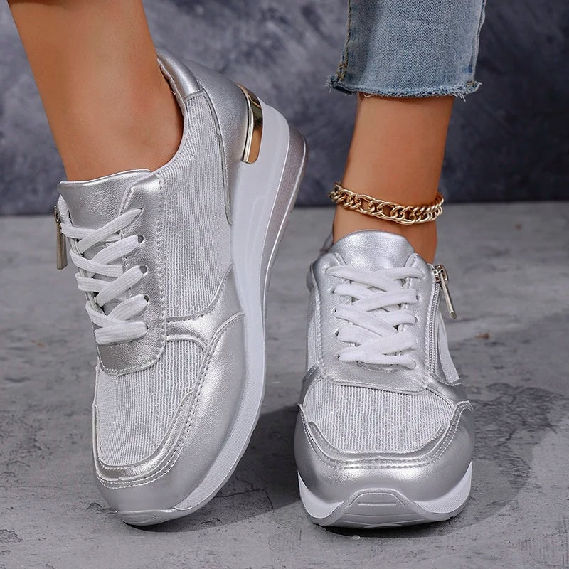 Silver metallic sneakers shown from the front and side, highlighting the lace-up design, side zips, and textured outsoles.