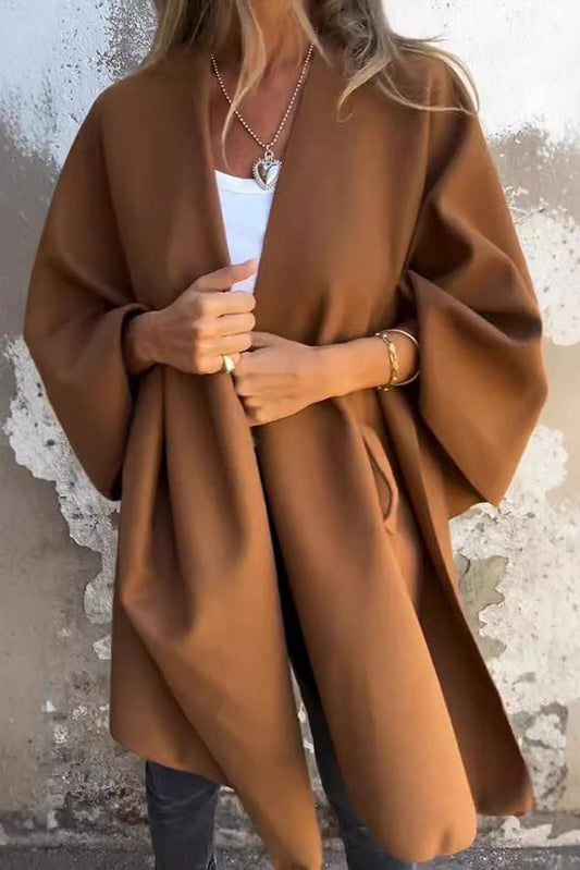 Brown open-front cape jacket with flowing hip-covering panels and wide three-quarter sleeves, worn over a white top.