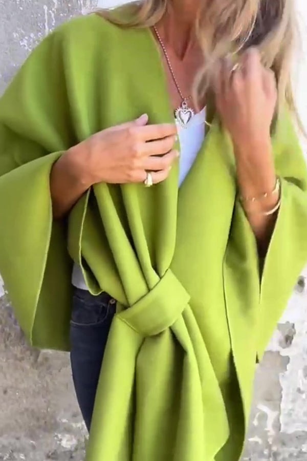 Olive green open-front cape jacket shown with its long front drape and wide sleeve while worn over a white top.