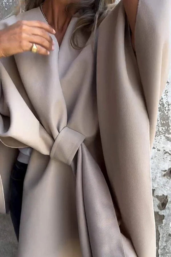 Taupe cape jacket shown in close view with a tied front, layered panels, and a broad draped sleeve.