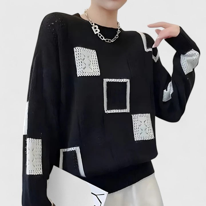 Black crew neck sweater with white openwork and contrasting patchwork squares arranged across the front and sleeves.