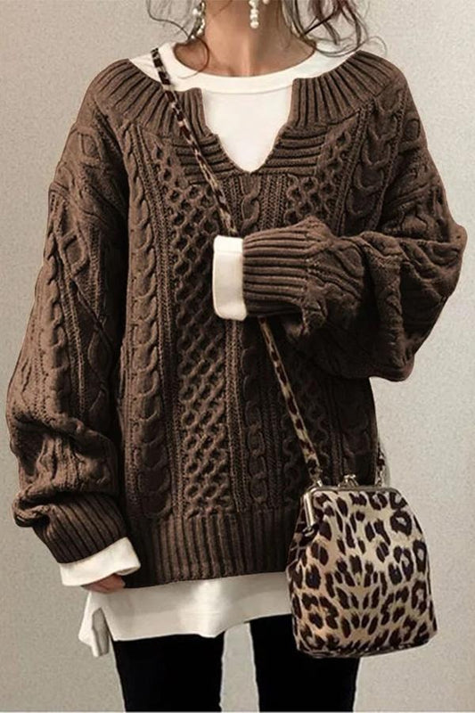 Brown oversized cable knit V-neck sweater with long sleeves and ribbed cuffs, layered over a white longline top.