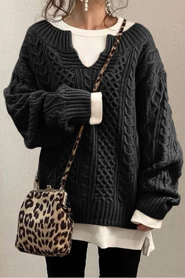 Black oversized V-neck sweater with prominent cable knit texture, long sleeves, and a ribbed hem over a white top.