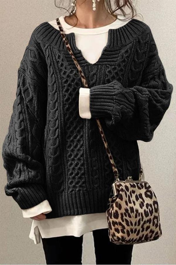 Black longline cable knit V-neck sweater shown with its oversized silhouette and gathered ribbed sleeve cuffs.