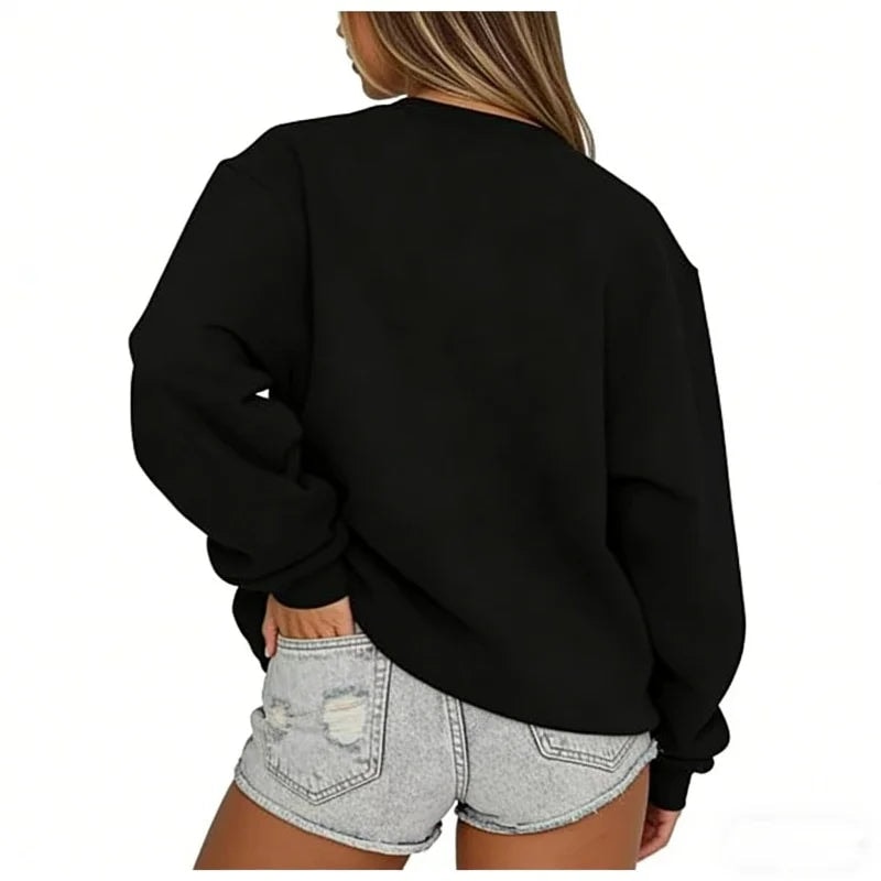 Back view of the black oversized sweatshirt, showing its relaxed shape, long sleeves, and ribbed hem above denim shorts.