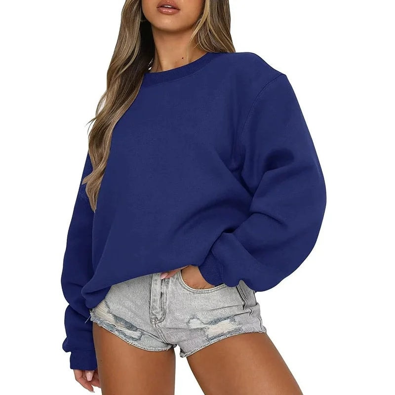 Front view of the oversized sweatshirt in deep blue, styled with light denim shorts and one hand in a pocket.