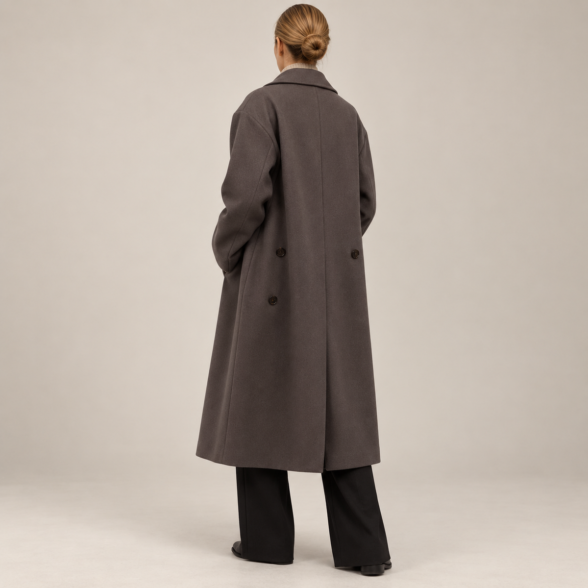 Back view of the taupe below-the-knee coat, showing its relaxed oversized shape, center back seam, and rear button details.