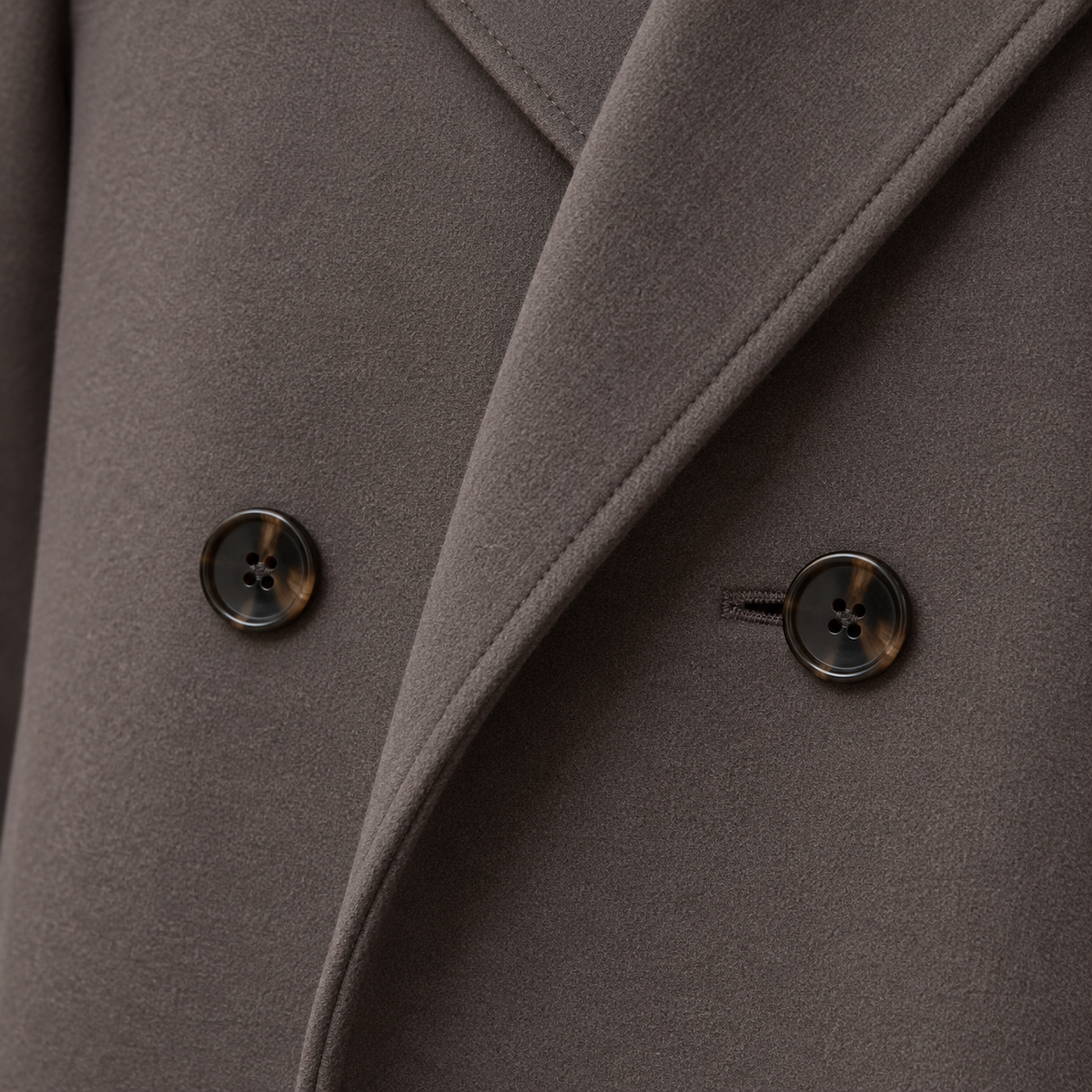 Detailed close-up of the overlapping front panels and two dark buttons on the taupe double-breasted coat.