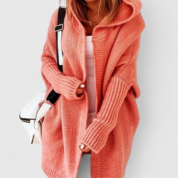 Coral oversized open-front cardigan styled over a light top, showing the roomy hood, long sleeves, and extended relaxed length.