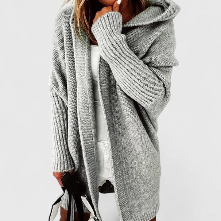 Gray hooded cardigan worn open over a light outfit, with one sleeve raised and the long front panels hanging freely.