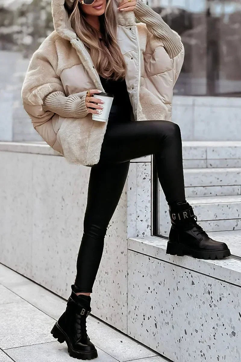 Light neutral oversized hooded puffer jacket styled with its front secured, displaying the contrasting plush panels and generous hood.