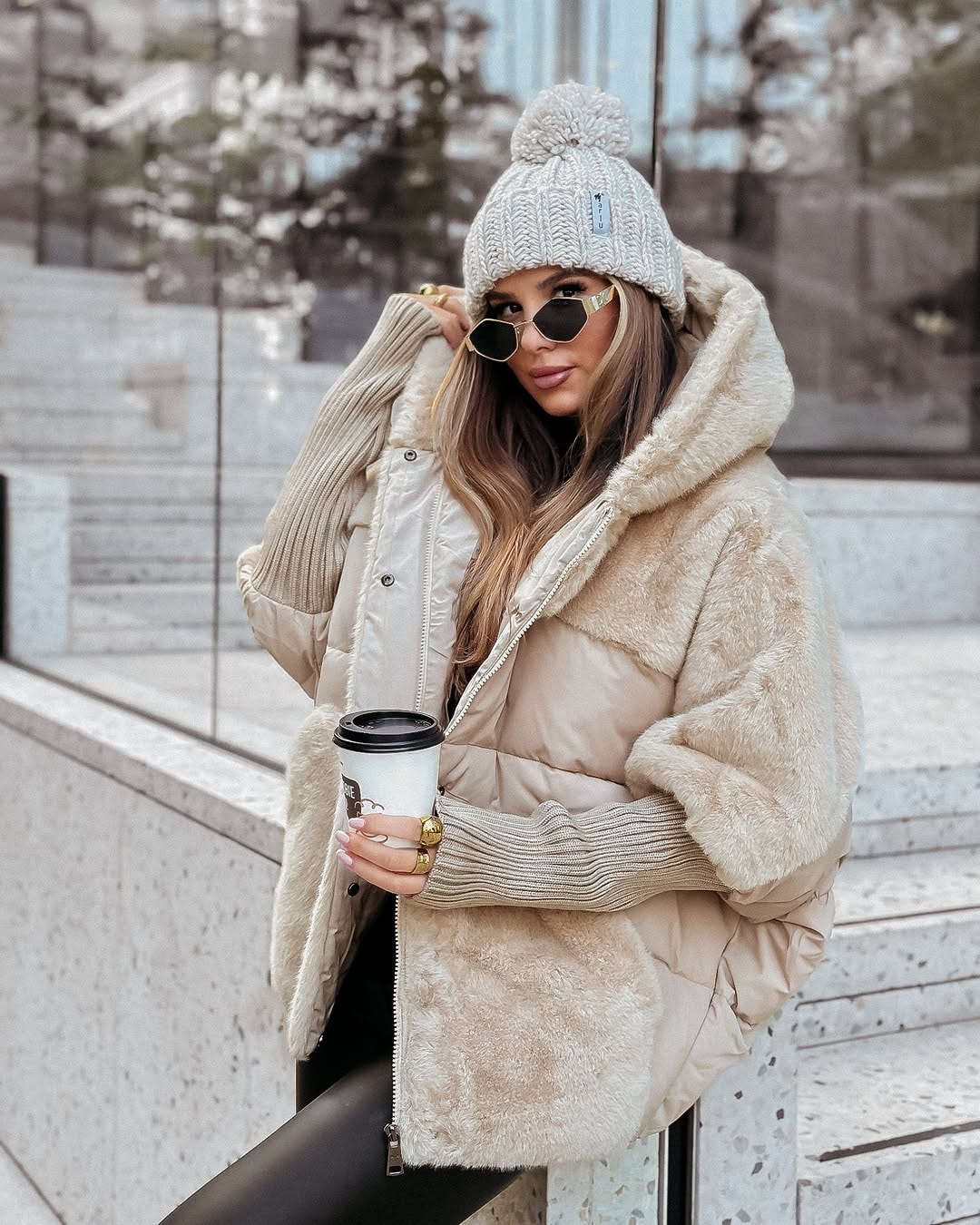 Light neutral oversized puffer jacket with a plush-lined hood, contrasting textured panels and ribbed sleeve cuffs.