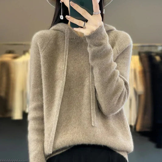 Taupe oversized knit pullover hoodie with long drawstrings, long sleeves, and ribbed cuffs, styled with dark trousers.