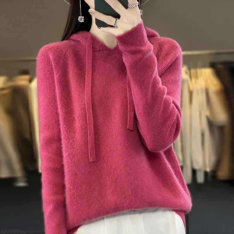 Berry-pink oversized knit hoodie with a roomy pullover fit and long drawstrings, paired with light trousers.
