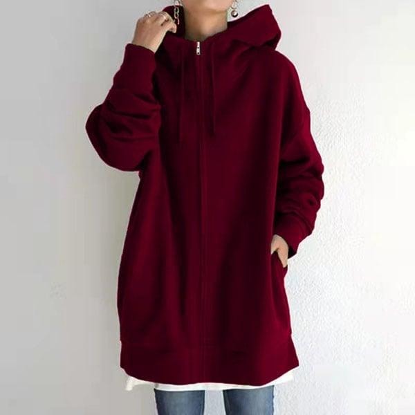 Front view of the burgundy oversized zip-up hoodie worn over a white top, with one hand touching the hood and the other in a pocket.