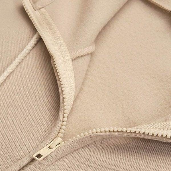 Close-up of the beige hoodie showing the front zipper, zipper pull, hood seam, and soft-looking inner surface.