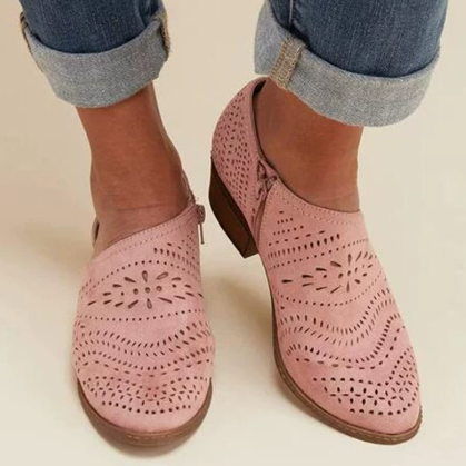 Pair of pink perforated ankle boots with rounded toes and low block heels, styled with cuffed jeans.