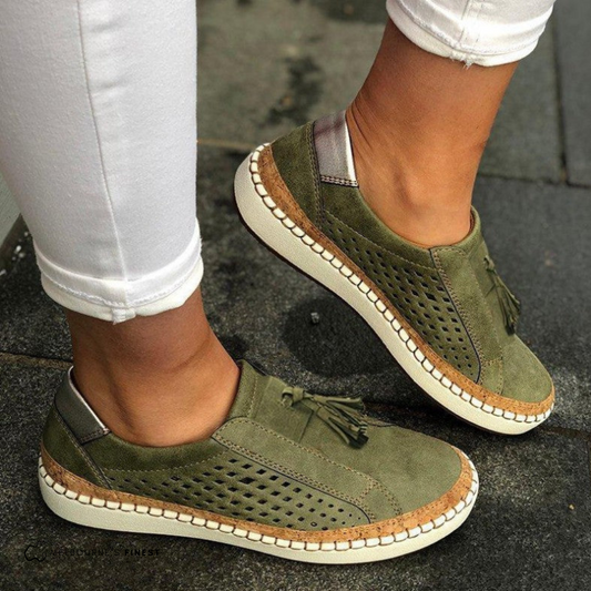 Olive green perforated slip-on sneakers with decorative front tassels and contrasting stitched soles, shown worn with white cropped jeans.