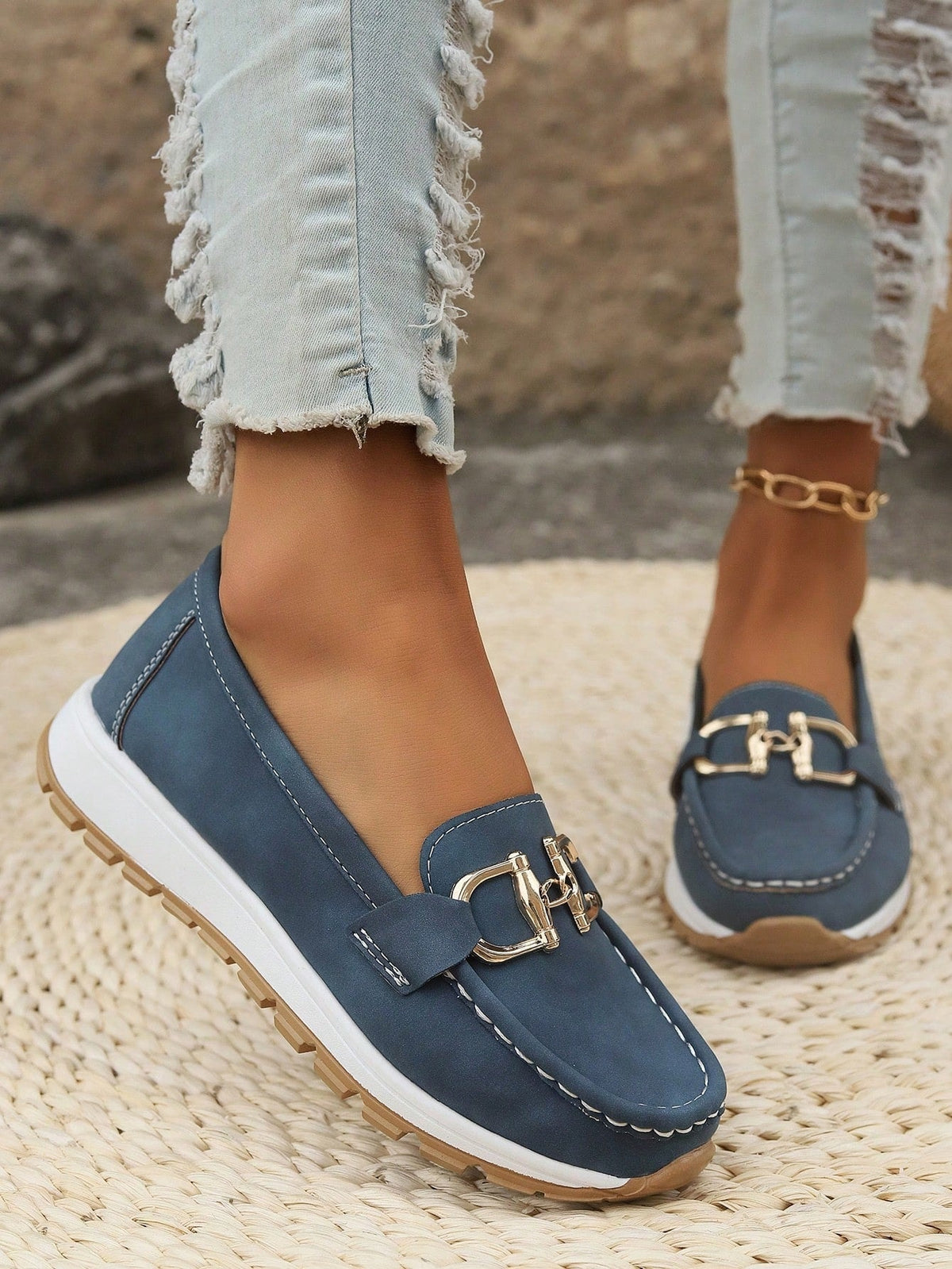 Navy blue slip-on loafers with white stitching, raised white soles, textured outsoles, and a prominent gold-tone buckle.