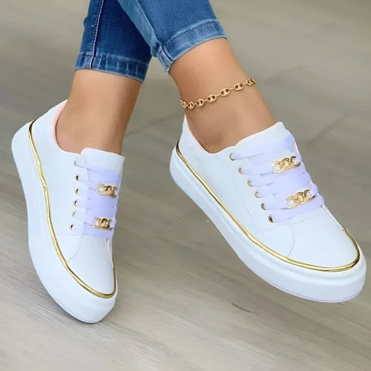 White platform sneakers with lace-up fronts, rounded toes, gold-tone chain accents, and metallic edging, shown with rolled jeans.