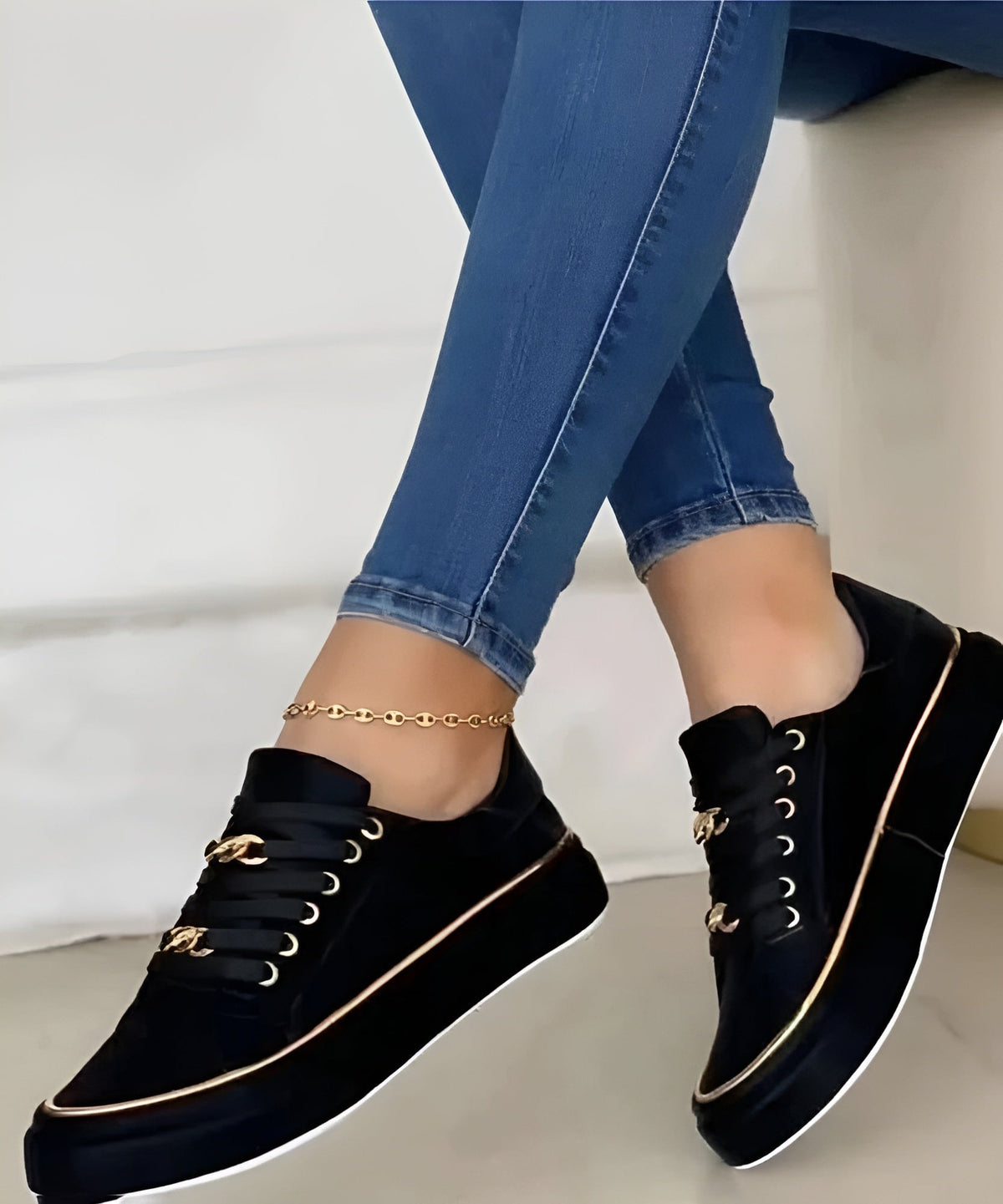 Black platform sneakers with gold-tone chain details on the laces and metallic trim, paired with fitted jeans.